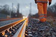 © Maris - A worker in high-visibility orange attire stands by the illuminated railway track at dusk, signifying hard work, safety, and dedication in a detailed composition.
