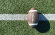 © Angelov - Close up of an american football on the field, players in the background