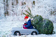 © Irina Schmidt - Happy little smiling girl driving toy car with Christmas tree. Funny preschool child in winter clothes bringing hewed xmas tree from snowy forest. Family, tradition, holiday.
