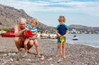 © Irina Schmidt - Happy grandfather and two little kid boys playing together on beach and building sand and stone castle. Beautiful family enjoying vacations on sea and ocean, granddad and children