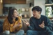 © munja02 - An Asian couple having an argument at home, sitting on the sofa in their living room and arguing with each other while gesturing animatedly, both looking angry