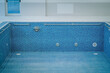 © Raivo - Empty indoor pool with blue mosaic tiles, metal handrails, and wall vents. The space is well-lit and offers ample copy space..
