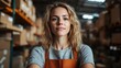 © Larisa AI - A self-assured woman stands confidently in a bustling warehouse, wearing an orange apron, surrounded by shelves filled with stacked boxes of inventory products.