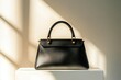 © Viktor Petrushenko - Elegant black leather handbag displayed on a pedestal with soft, warm sunlight casting shadows.
