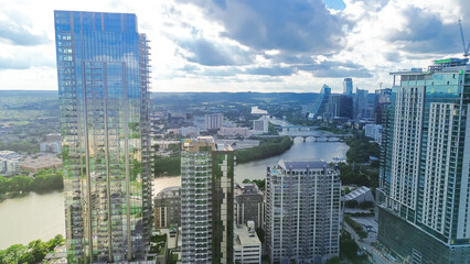  Aerial view Austin Downtown skyscrapers along lush green curved Colorado River, high rise office buildings under construction, fast growing Texas Capital City, modern skyline hotel condos