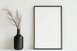 © VERTEX SPACE - Minimalist decor featuring black vase with dried grass and blank picture frame against neutral wall. This serene setup adds touch of elegance to any space