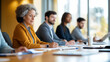 © Kateryna - A team of business professionals sits at a long conference table during a strategy session in a modern office space. The image captures a senior woman jotting down notes, while her