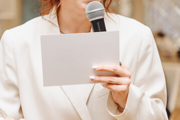 white blank paper card in hand of wedding or corporate presenter or event manager, young caucasian woman in white costume, mockup, copy space