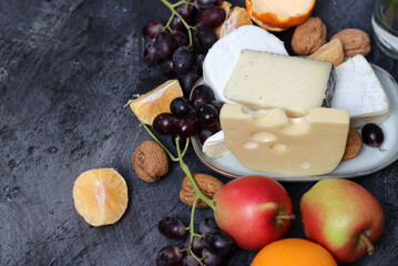 Still life with Dutch cheese and seasonal fruit on dark grey textured background with space for text. 