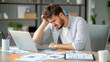 © songwut - Person hunched over a desk, with a laptop open and a pile of work, showing stress