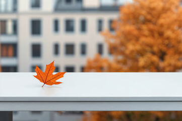 Poster - Single orange maple leaf lying on empty white table with defocused cityscape background