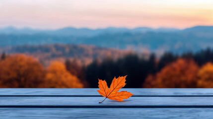 Poster - Single orange maple leaf lying on empty wooden table with blurred autumn forest in background