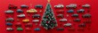© Maria Mikhaylichenko - Festive holiday scene featuring colorful toy cars arranged around a miniature Christmas tree, creating a unique and playful automotive-themed seasonal display on a bright red background.