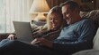 © Nathan - Smiling middle-aged couple enjoying time together while using a laptop on a cozy couch, bathed in warm light.
