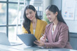 © Tj - Two young businesswomen smiling, reviewing a contract in a modern office. Working together, focused on discussion, showcasing professionalism. Bright space with laptop and documents