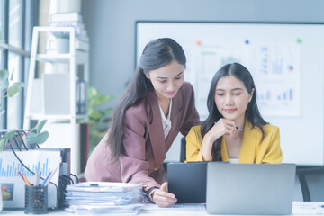 two asian businesswomen are having a discussion while working together on a laptop in a modern offic