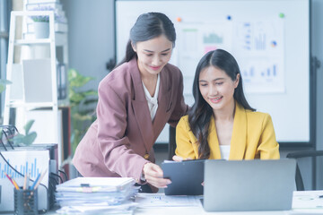 Two asian businesswomen deeply engrossed in discussing a new project, collaborating and planning surrounded by documents and technology, exuding confidence and happiness in a modern office setting