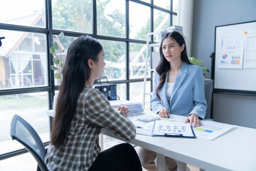 Two asian businesswomen are discussing financial data and charts during a meeting in a modern office. They are working together to analyze the company's performance