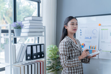 Focused asian businesswoman analyzing charts at desk in modern office, exuding confidence and determination for financial success