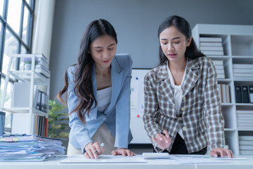 two young businesswomen are working together over a table, going through paperwork and using a calcu