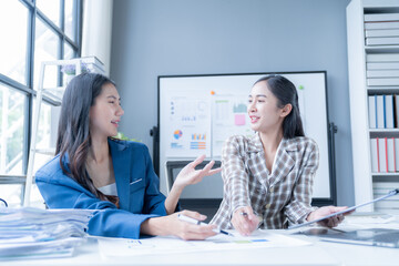 Two asian businesswomen are having a productive meeting, discussing financial charts and analyzing market trends. They are working together in a modern office