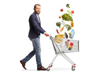 Wall Mural - Bearded guy walking and pushing a shopping cart with groceries falling