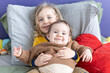 © Valmedia - Smiling little boy is hugging her happy baby sibling on a bed with colorful pillows and blankets. Selective focus