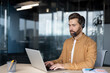 © Liubomir - Professional man wearing headset works on laptop in modern office. Glass walls and natural light create a bright environment enhancing focus, concentration, communication, productivity.