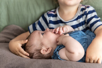 Big brother is holding his baby sister and caressing her head while she plays with her fingers. Selective focus