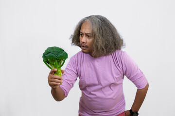 curly-haired Asian adult male carrying a tray of fresh vegetables while pointing at it, healthy and nutritious fresh vegetables eating campaign, healthy lifestyle