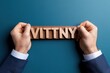 © JK_kyoto - Hands holding a wooden sign with the word VITTNY against a teal background, symbolizing branding and communication.