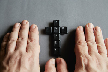 Computer keys with the letters M, O, N, E, Y and J, O, B form a cross next to two human hands on a gray background, only business, the word 