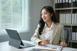 © amnaj - Young businesswoman is reviewing data and smiling while working in her office