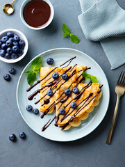 Wall Mural - Crepes, thin pancakes with chocolate sauce and fresh blueberries. Grey background. Top view.