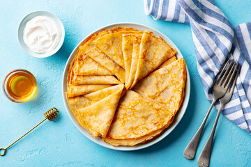 Wall Mural - Crepes, thin pancakes on a plate with honey and cream. Blue background. Top view.