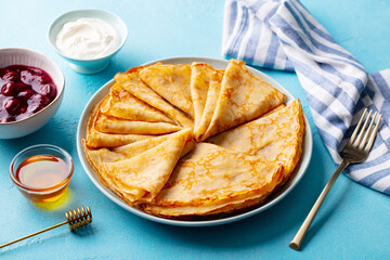 Wall Mural - Crepes, thin pancakes on a plate with honey and cream. Blue background. Close up.