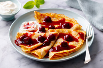 Wall Mural - Crepes, thin pancakes with cherry, berry sauce and whipped cream. Marble table background. Close up.