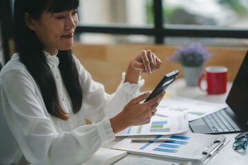 Focused businesswoman calculating expenses in office surrounded by paperwork, laptop, smartphone, and calculator, sipping coffee. Confident and happy, she plans for growth