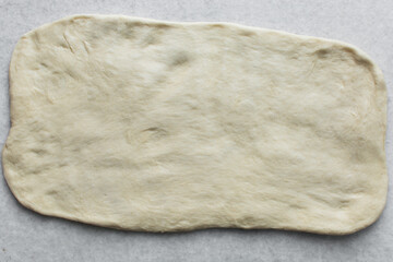 Overhead view of challah dough flattened on a white granite countertop, top view of homemade challah dough on white countertop, process of making challah