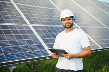 an indian male engineer working on a field of solar panels. the concept of renewable energy