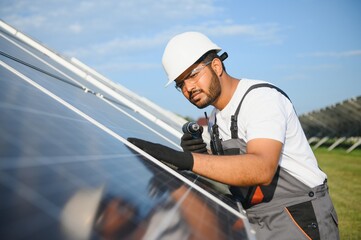 Indian man in uniform on solar farm. Competent energy engineer controlling work of photovoltaic cells