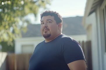 A man in casual attire gazes into the distance, reflecting while standing in a sunlit backyard