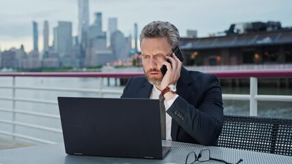 Wall Mural - Business man working online on laptop and talking on phone outdoor. Business talk. Busy businessman talking on phone. Man send business email and surf on laptop and using smart phone.