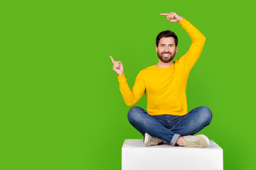 Poster - Full size photo of pretty young male point empty space sit cube wear trendy yellow outfit isolated on green color background