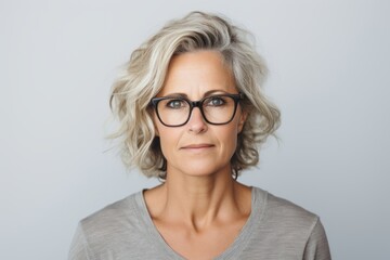 Serious mature woman in eyeglasses looking at camera while standing against grey background