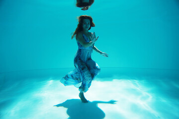 Young woman in blue dress underwater in the pool