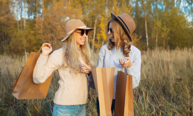 Wall Mural - Fashionable happy young two women friends with shopping bags, stylish smiling girlfriends in park