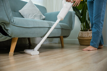 Housewife female dust cleaning floor under sofa or couch furniture with vacuum cleaner, Happy Asian young woman with accumulator vacuum cleaner at home in living room, household and housework concept