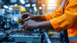 © Maksym - A close-up of a mixed-race female construction apprentice's hands as she expertly handles tools and wires in a busy industrial factory, the blurred background providing copy space
