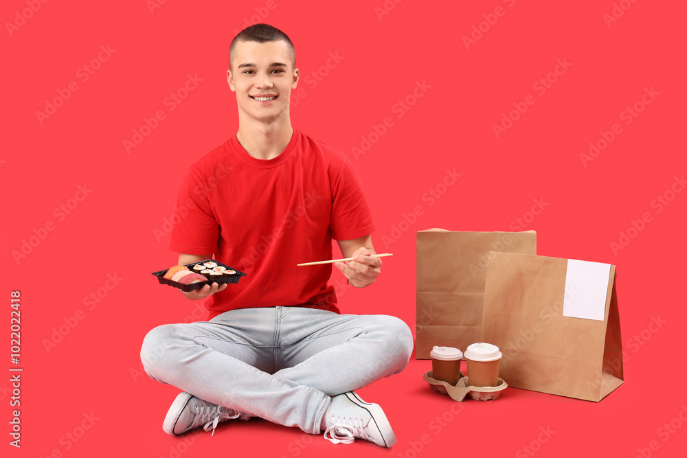 Young man eating tasty sushi on red background